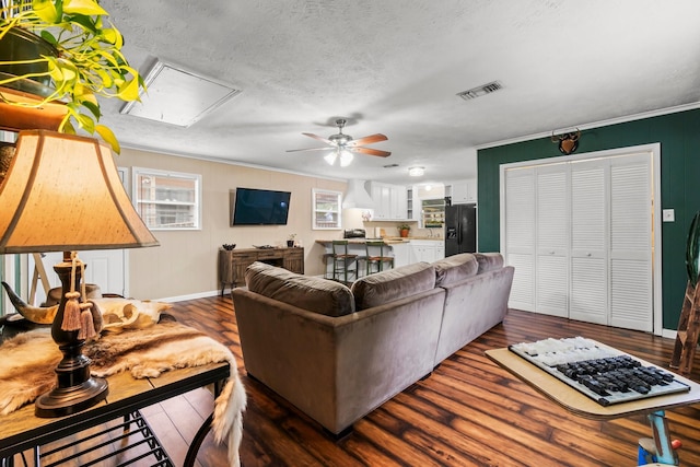 living room with ceiling fan, dark wood-type flooring, a textured ceiling, and ornamental molding