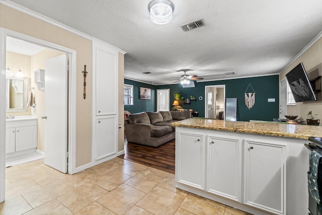 kitchen featuring ceiling fan, light stone counters, a textured ceiling, white cabinets, and ornamental molding