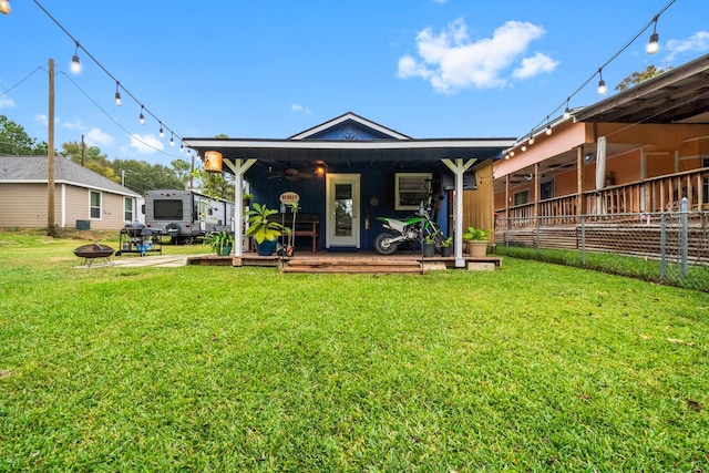 back of property with a wooden deck, ceiling fan, a yard, and a fire pit