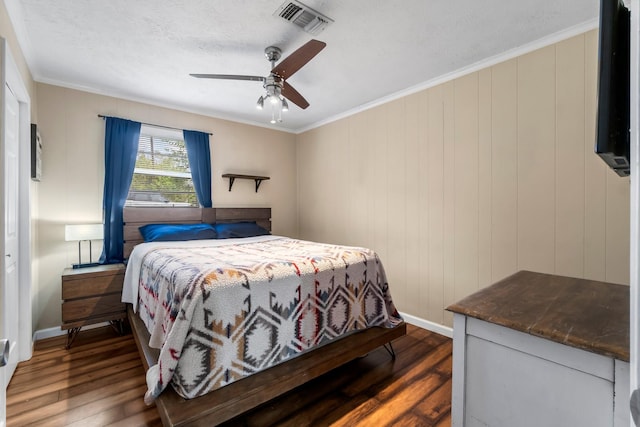 bedroom with dark wood-type flooring, wooden walls, ceiling fan, ornamental molding, and a textured ceiling