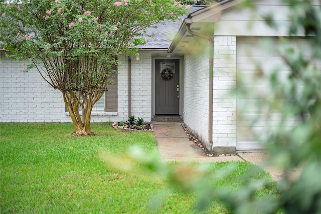 view of exterior entry featuring brick siding, a lawn, and a shingled roof