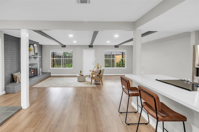 dining room with beam ceiling, light hardwood / wood-style flooring, a healthy amount of sunlight, and a brick fireplace