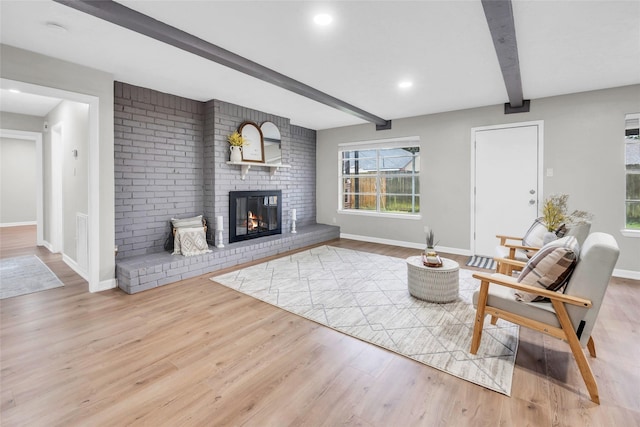 living room with beam ceiling, light wood-type flooring, and a brick fireplace