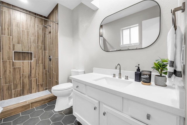 bathroom with tile patterned flooring, vanity, toilet, and tiled shower