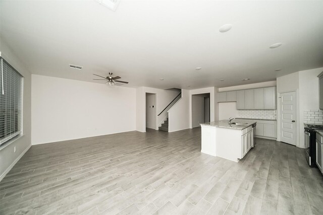 kitchen with decorative backsplash, light wood-type flooring, ceiling fan, a center island with sink, and stainless steel stove