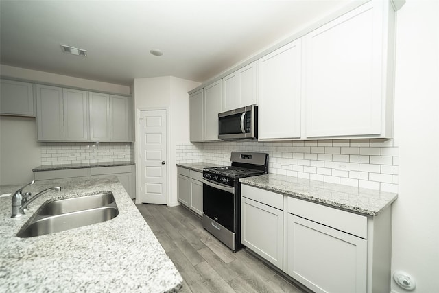 kitchen featuring light stone countertops, sink, decorative backsplash, appliances with stainless steel finishes, and light wood-type flooring