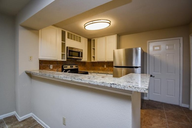 kitchen with kitchen peninsula, backsplash, light stone counters, stainless steel appliances, and white cabinets