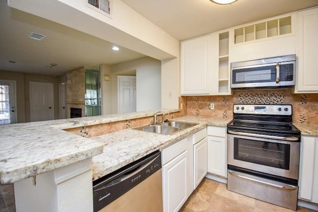 kitchen featuring kitchen peninsula, appliances with stainless steel finishes, light stone counters, sink, and white cabinetry