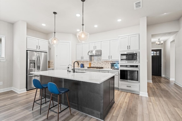 kitchen featuring white cabinets, light wood-type flooring, stainless steel appliances, and a kitchen island with sink