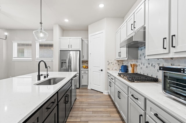 kitchen featuring stainless steel appliances, sink, decorative light fixtures, white cabinets, and light hardwood / wood-style floors