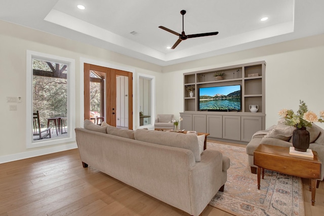 living room with a tray ceiling, ceiling fan, and light wood-type flooring