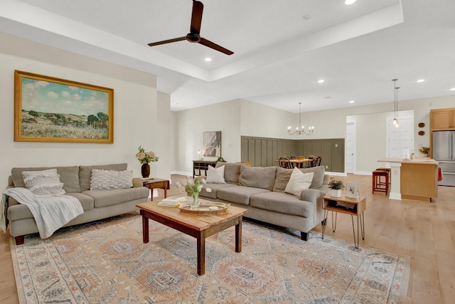 living room with a raised ceiling, light hardwood / wood-style flooring, and ceiling fan with notable chandelier