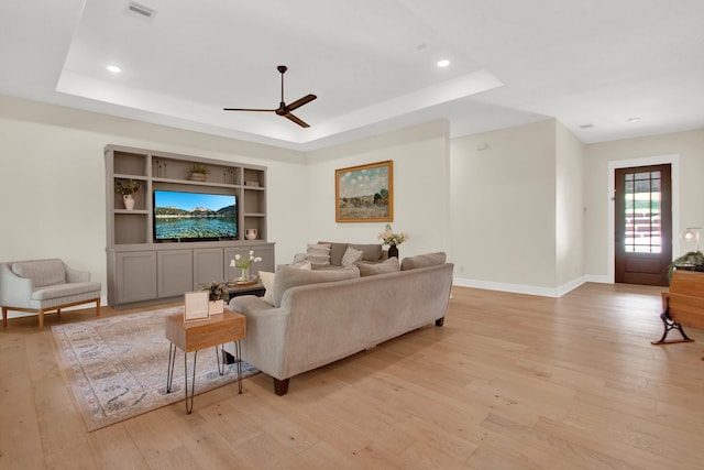 living room featuring ceiling fan, a raised ceiling, and light wood-type flooring