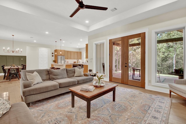 living room featuring ceiling fan with notable chandelier, french doors, a tray ceiling, and light hardwood / wood-style flooring