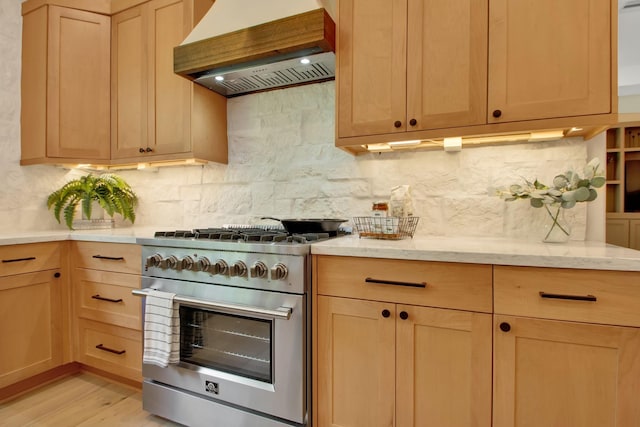 kitchen featuring tasteful backsplash, light brown cabinetry, custom exhaust hood, high end stainless steel range, and light wood-type flooring