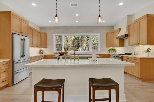 kitchen featuring light stone countertops, stainless steel appliances, light hardwood / wood-style floors, a kitchen island with sink, and custom exhaust hood