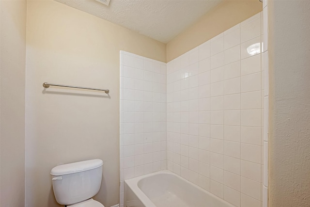 bathroom featuring tiled shower / bath, a textured ceiling, and toilet