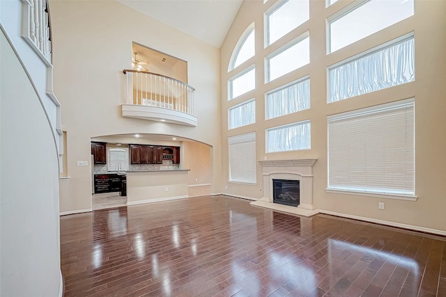 unfurnished living room with sink, a towering ceiling, and wood-type flooring