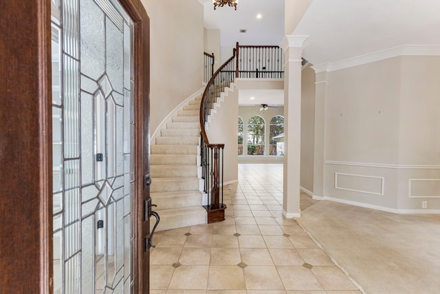 foyer featuring light carpet, ceiling fan with notable chandelier, crown molding, a towering ceiling, and decorative columns