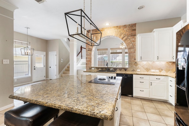 kitchen with light stone countertops, ceiling fan with notable chandelier, black appliances, a center island, and white cabinetry