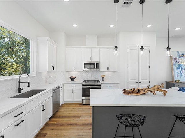 kitchen with sink, light wood-type flooring, appliances with stainless steel finishes, decorative light fixtures, and white cabinetry