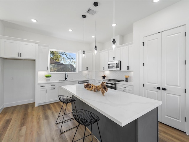 kitchen featuring appliances with stainless steel finishes, sink, a center island, white cabinetry, and hanging light fixtures