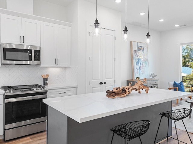 kitchen featuring appliances with stainless steel finishes, a kitchen breakfast bar, pendant lighting, white cabinets, and a center island