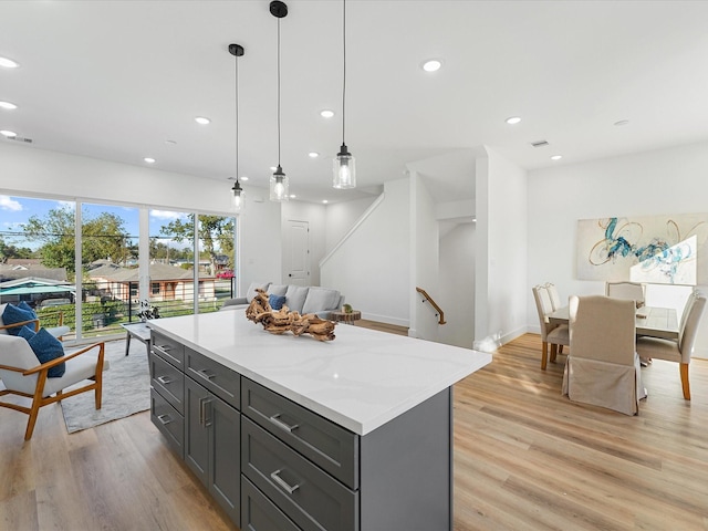 kitchen with pendant lighting, a center island, light stone countertops, and light wood-type flooring