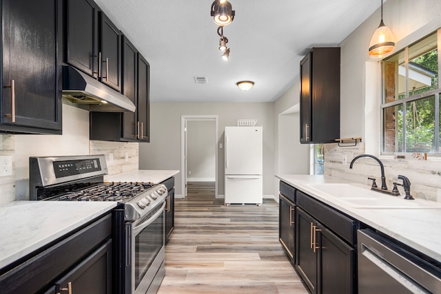 kitchen with sink, tasteful backsplash, light hardwood / wood-style flooring, decorative light fixtures, and appliances with stainless steel finishes