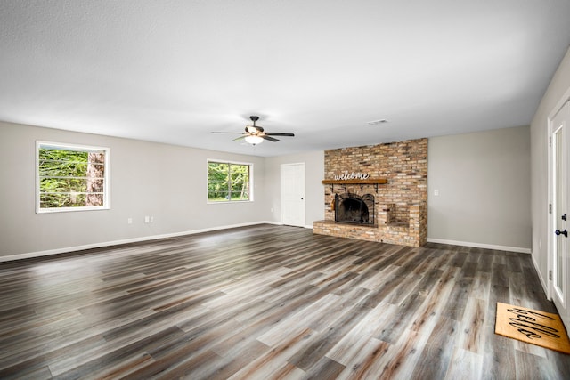 unfurnished living room with dark hardwood / wood-style floors, a brick fireplace, plenty of natural light, and ceiling fan