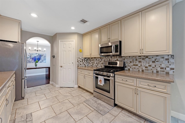 kitchen with cream cabinetry, appliances with stainless steel finishes, backsplash, and a chandelier