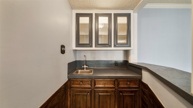 bar with sink, wood walls, a textured ceiling, dark brown cabinets, and ornamental molding