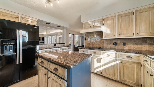 kitchen featuring light tile patterned flooring, dark stone counters, black appliances, a textured ceiling, and a kitchen island