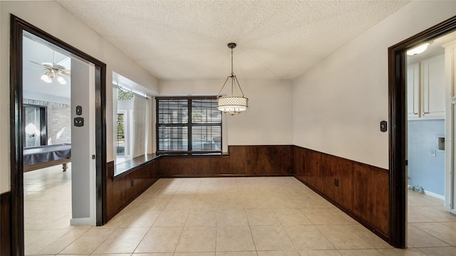 unfurnished dining area featuring ceiling fan, wood walls, light tile patterned flooring, and a textured ceiling