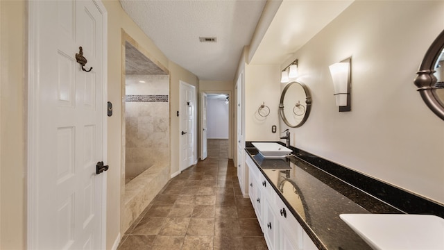 bathroom featuring vanity, a textured ceiling, and tiled shower