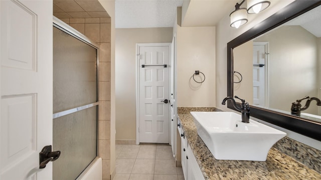 bathroom with a textured ceiling, vanity, tile patterned floors, and bath / shower combo with glass door