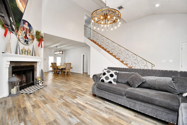 living room with a chandelier, hardwood / wood-style floors, high vaulted ceiling, and a tile fireplace