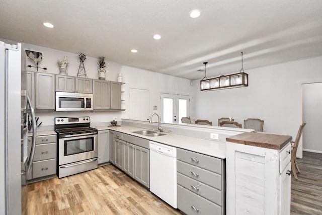 kitchen with kitchen peninsula, appliances with stainless steel finishes, light wood-type flooring, sink, and gray cabinets