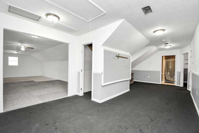 bonus room featuring a textured ceiling, ceiling fan, dark carpet, and vaulted ceiling