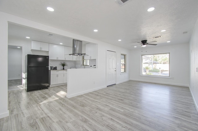 kitchen featuring white cabinetry, black refrigerator, wall chimney exhaust hood, and light hardwood / wood-style floors