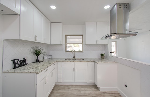 kitchen with white cabinets, light hardwood / wood-style flooring, wall chimney exhaust hood, and sink