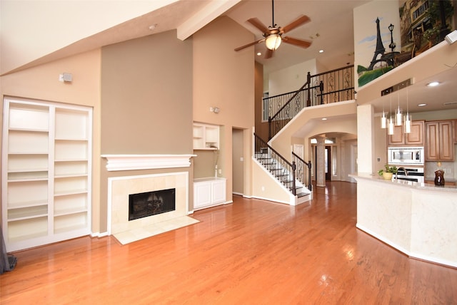 unfurnished living room featuring built in shelves, ceiling fan, sink, a high ceiling, and a tiled fireplace