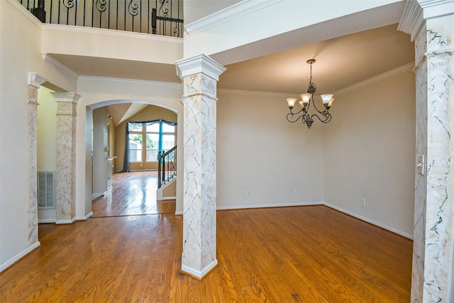 empty room featuring hardwood / wood-style flooring, a chandelier, crown molding, and decorative columns