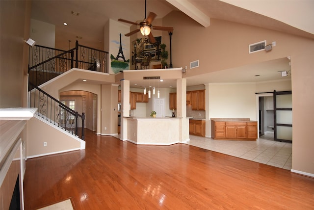 unfurnished living room with light wood-type flooring, ceiling fan, a barn door, high vaulted ceiling, and beamed ceiling