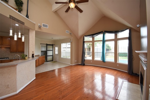 unfurnished living room with high vaulted ceiling, sink, ceiling fan, a barn door, and light wood-type flooring