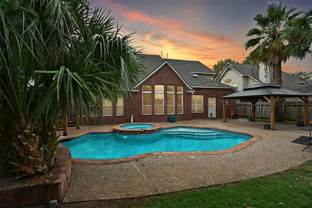 pool at dusk with a gazebo, a patio area, and an in ground hot tub