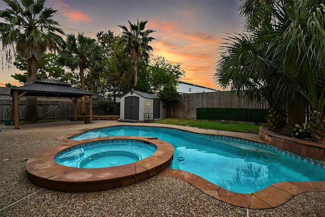 pool at dusk featuring an in ground hot tub, a gazebo, and a storage shed