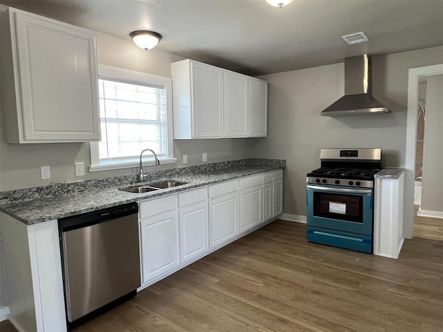 kitchen with hardwood / wood-style floors, white cabinets, wall chimney range hood, sink, and appliances with stainless steel finishes