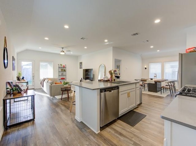 kitchen with sink, a kitchen island with sink, stainless steel appliances, light hardwood / wood-style floors, and white cabinets