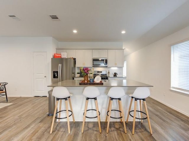 kitchen with a large island with sink, appliances with stainless steel finishes, white cabinets, and a kitchen breakfast bar